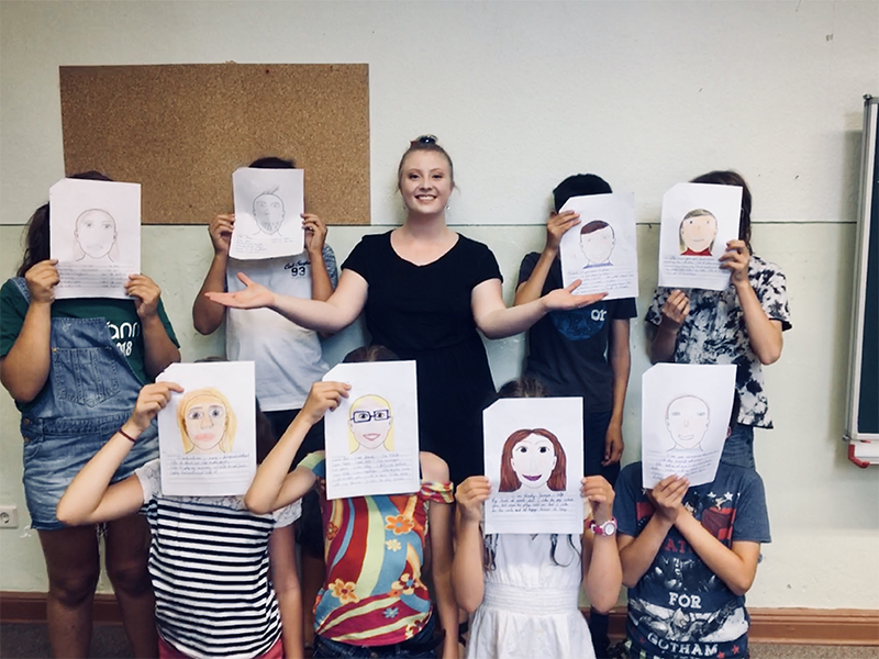 Erica Komp poses with German students who are holding their self portrait drawings