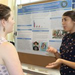Nicole Mejia speaks to a woman next to her Summer Scholars research poster