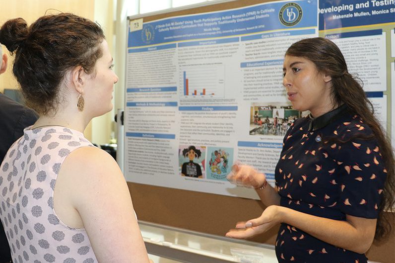 Nicole Mejia speaks to a woman next to her Summer Scholars research poster