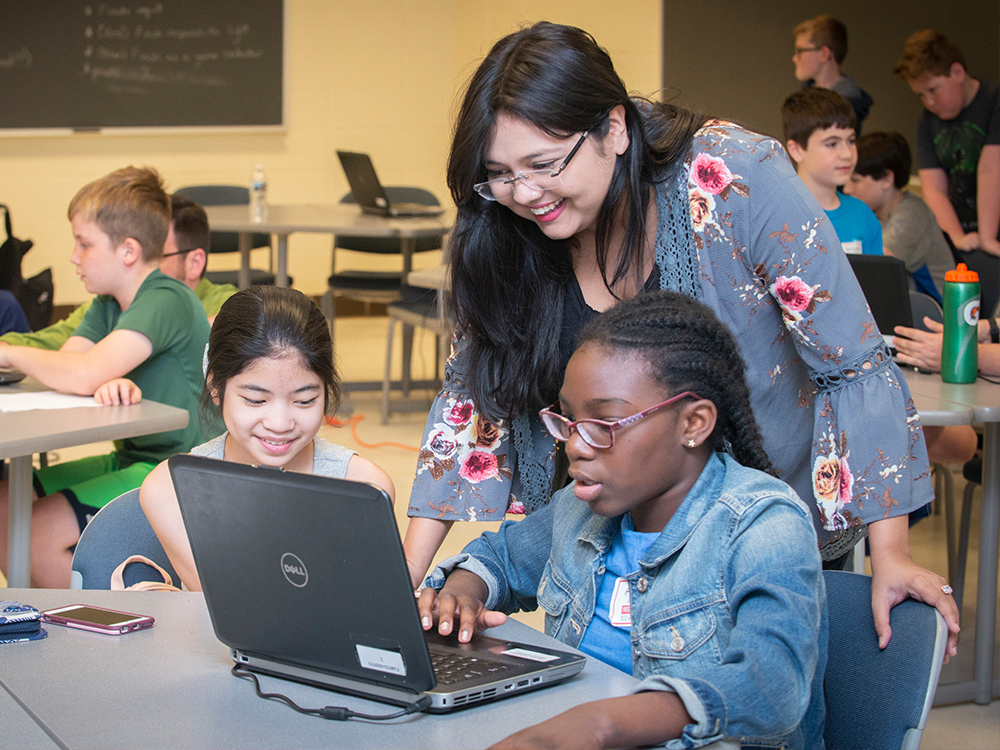 Teacher assists two students with a coding assignment
