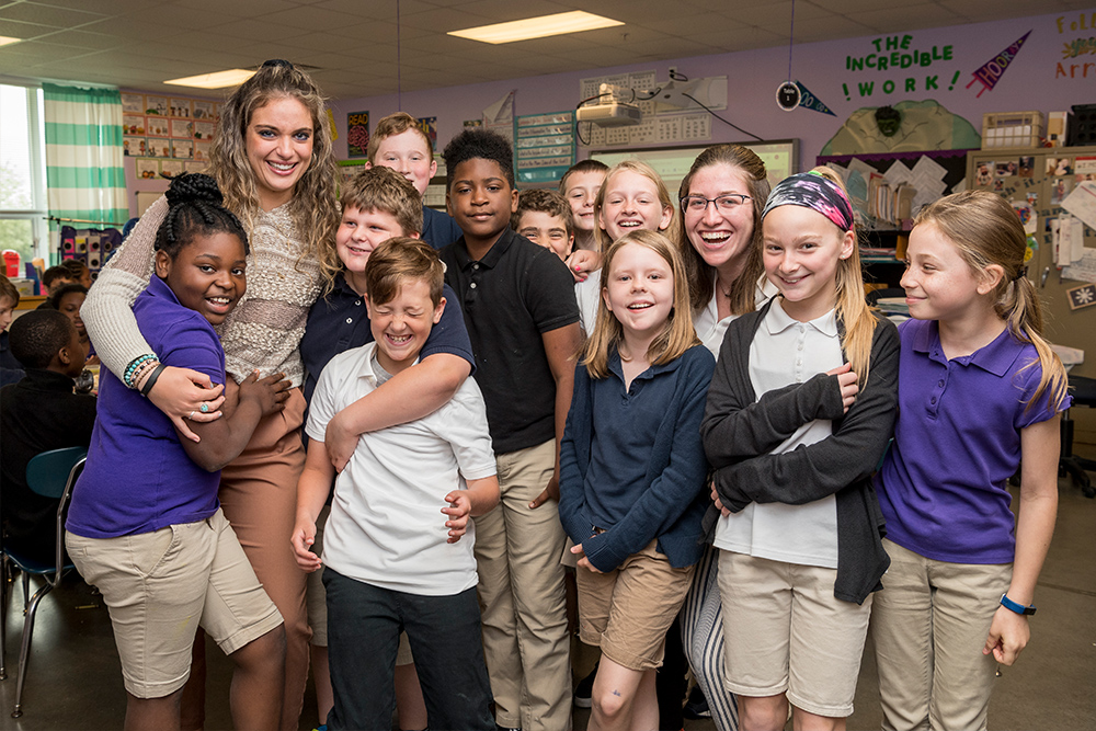 Two students teachers hug children in classroom