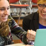 Two teachers have discussion while looking at a laptop