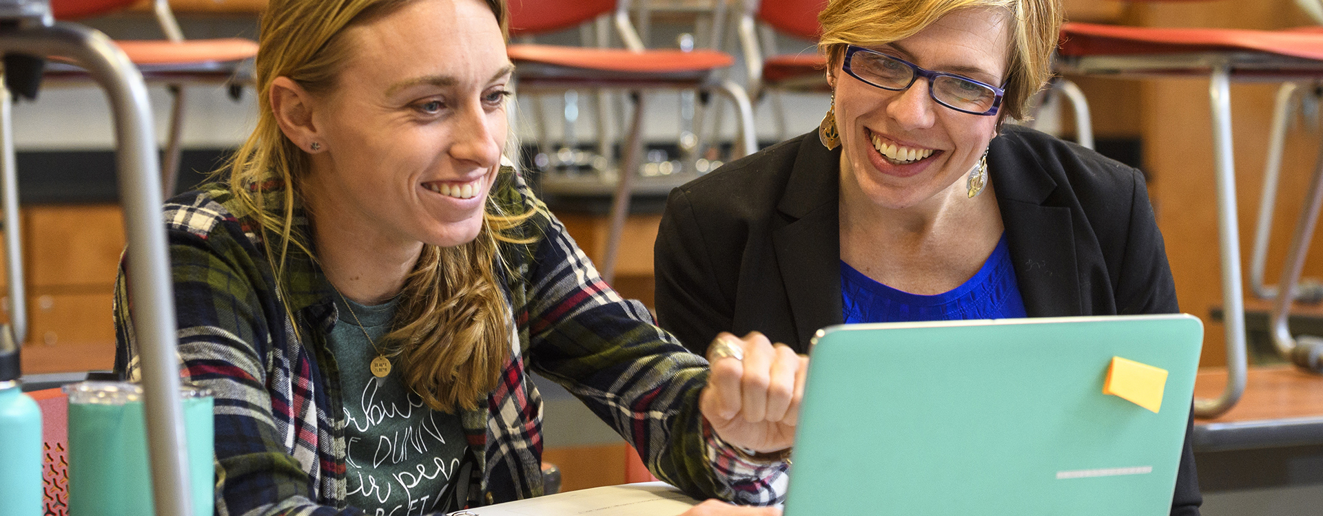 Two teachers have discussion while looking at a laptop