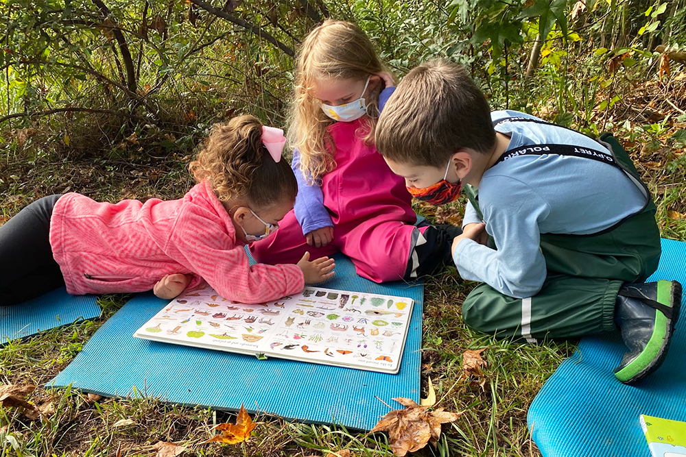 Three children reading a book outside at the UD Lab School