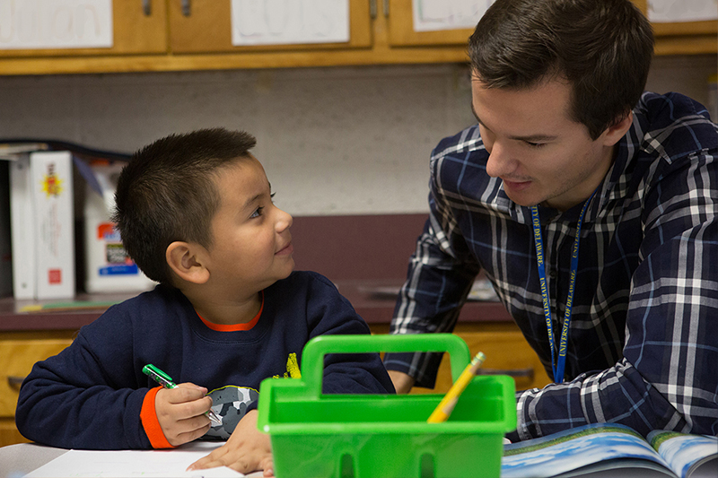 Student helping child with assignment in classroom