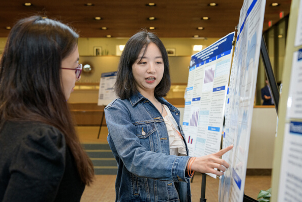 Doctoral student explaining research poster to another student