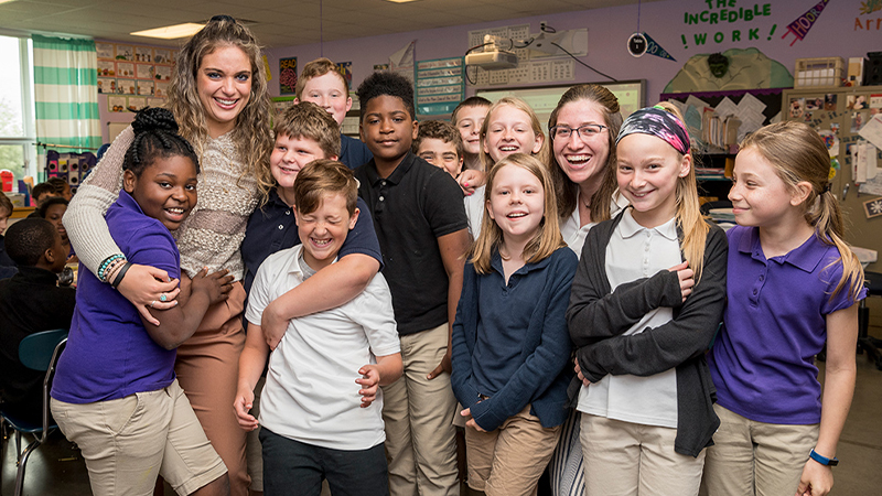 Two students teachers hug children in classroom