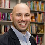 headshot of Joshua Wilson with books in the background