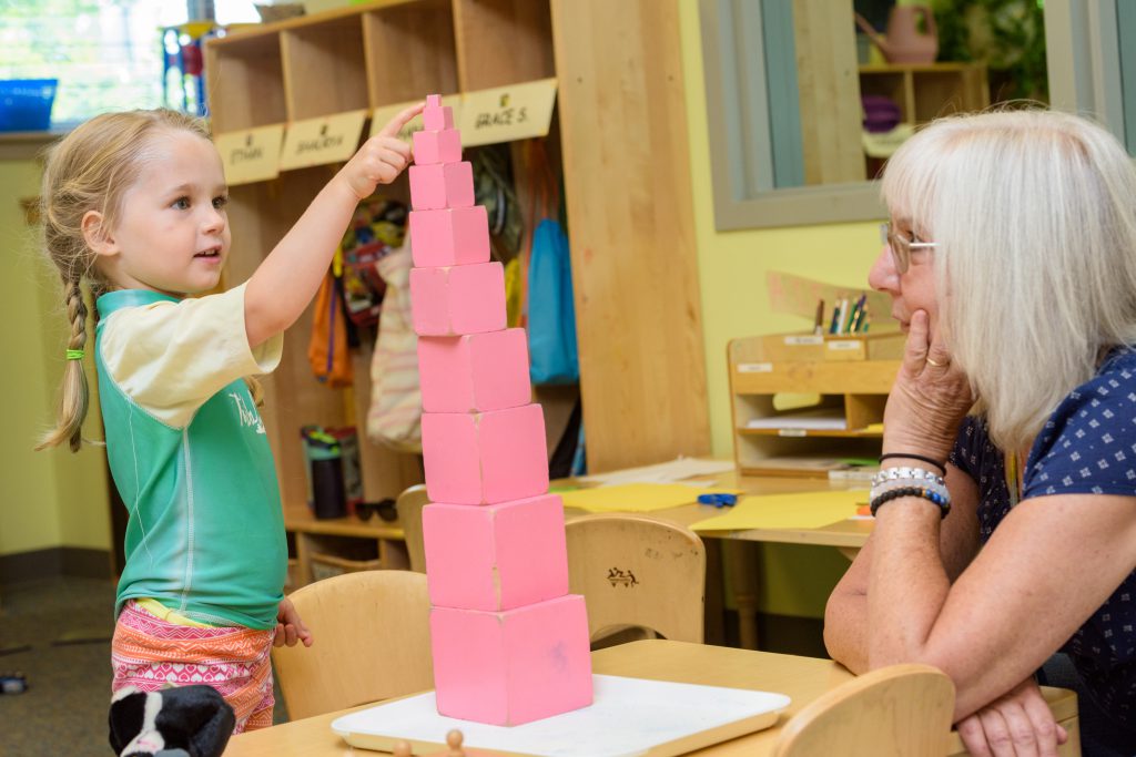 young female child and older woman play in classroom with pink building blocks