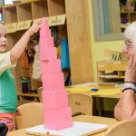 young female child and older woman play in classroom with pink building blocks
