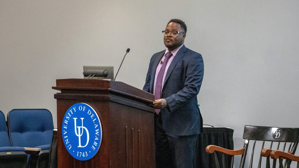 Matthew Patrick Steele standing in front of UD podium giving keynote talk at Steele Symposium