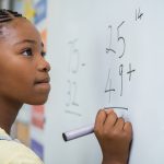 Young girl solving a math problem on a whiteboard