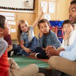 teacher sitting on the ground in classroom with a group of young students in a circle