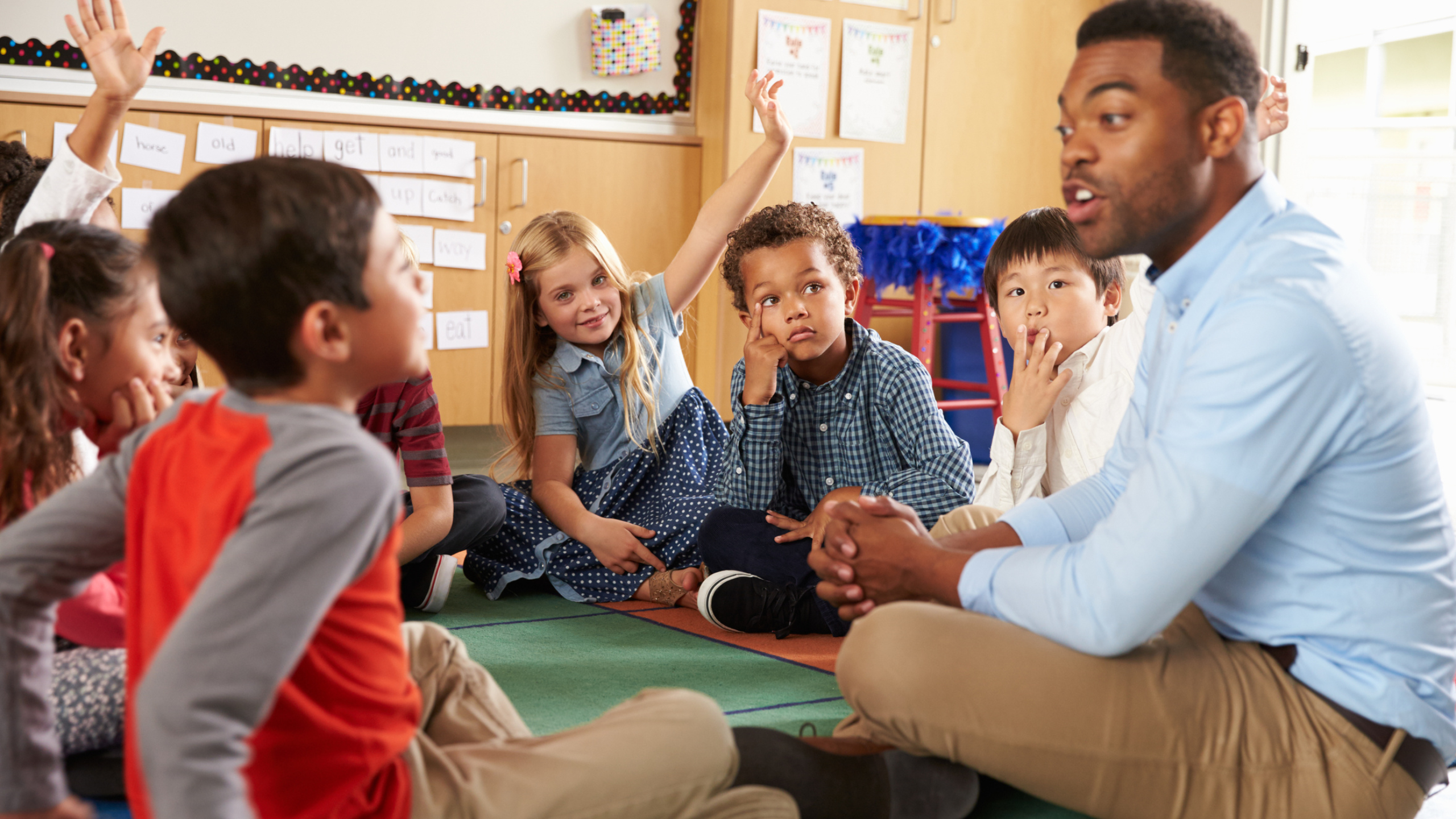 teacher sitting on the ground in classroom with a group of young students in a circle