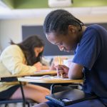 high school student writing at desk during Teachers of Tomorrow Summer Institute program.