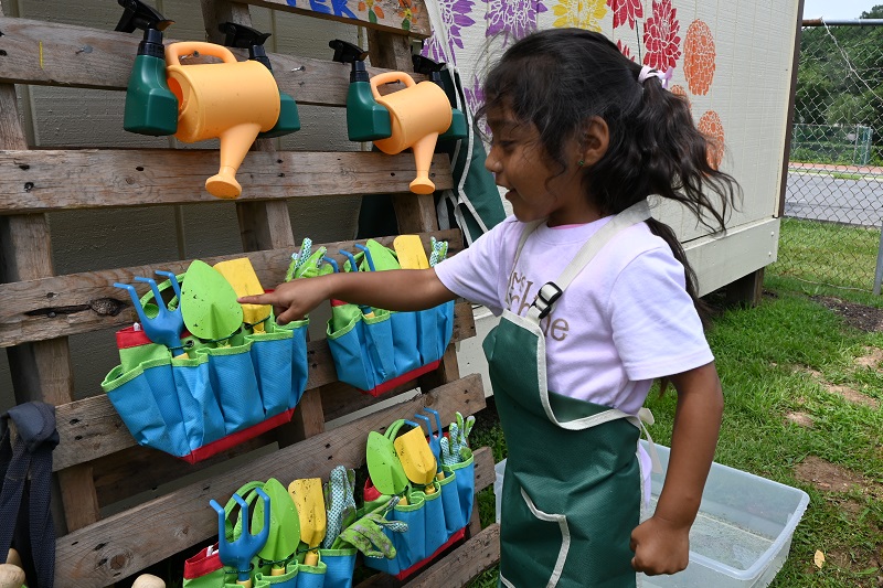 A child at Pirulo’s Child Care and Learning Center chooses a gardening tool in her outdoor gardening classroom.
