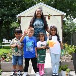 Diana Mercado, early childhood administrator at Pirulo’s Child Care and Learning Center, smiles with children in front of the garden she grew with the support of UD’s Let’s GROW Outside! initiative.