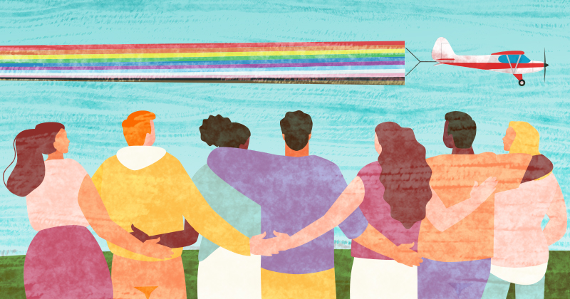 A group of people stand together looking at plane with a rainbow banner as it flies by.