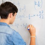 A student completes an algebra problem at the whiteboard.